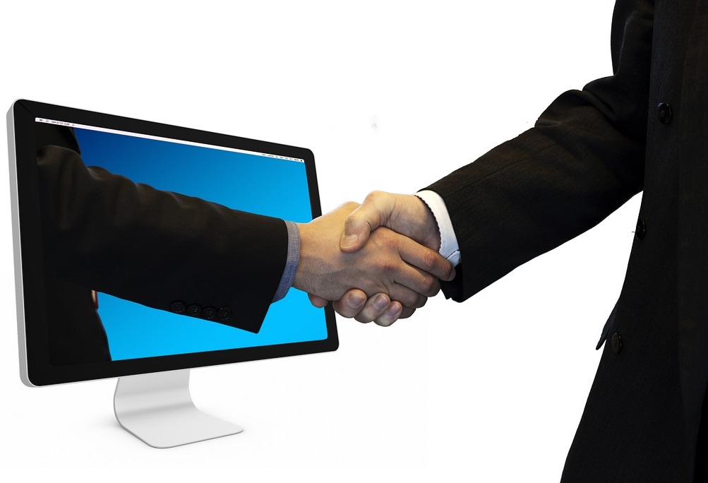 Händedruck zwischen zwei Geschäftspartnern, symbolisch durch einen Computerbildschirm, als Zeichen für digitale Zusammenarbeit und erfolgreiche Online-Geschäftsbeziehungen.